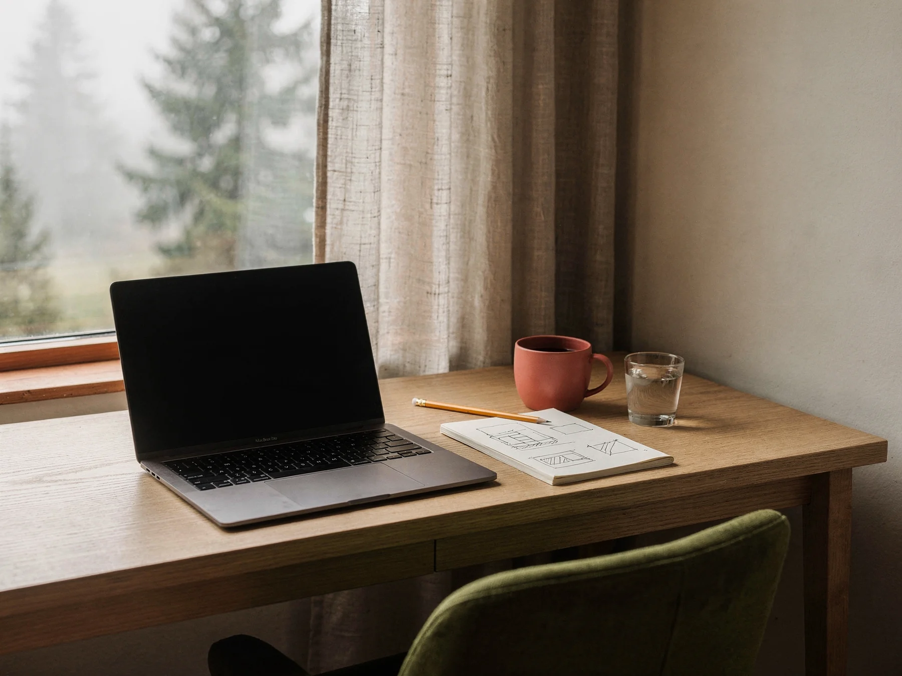 Illustrative designer workspace with a notebook, laptop, and natural window light
